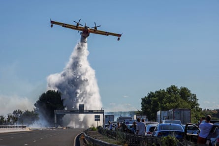People watch as a firefighting plane drops a payload of water on to a fire near a motorway