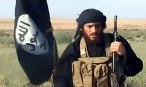 A man with a gun stands in front of a black flag