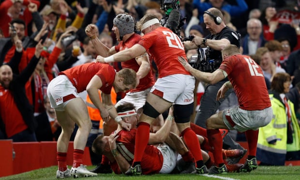Josh Adams (No 11) is mobbed by his Wales teammates after his late try sealed victory.