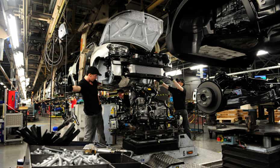 A Nissan employee working on the front end of a half-assembled car on a production line