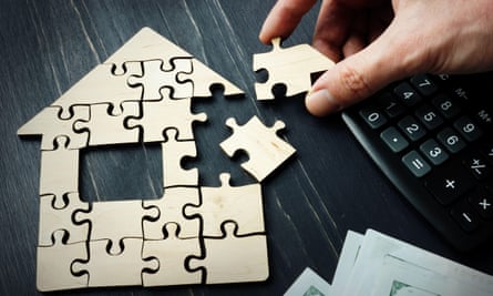 A hand puts together a house jigsaw, with a calculator next to it
