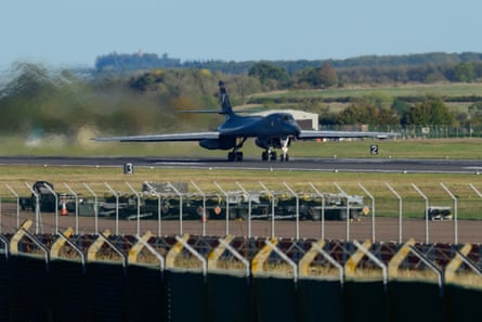 Munitions sit beside the runway as a Rockwell B-1 Lancer heavy bomber accelerates along the runway