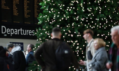People stand in front of a Christmas tree with a departures board behind it