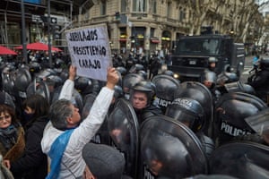 A man holds up a cardboard sign in front of a barricade of riot police