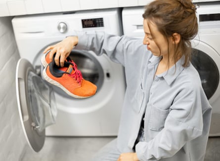 Woman grimacing as she puts sport shoes into the washing machine at home