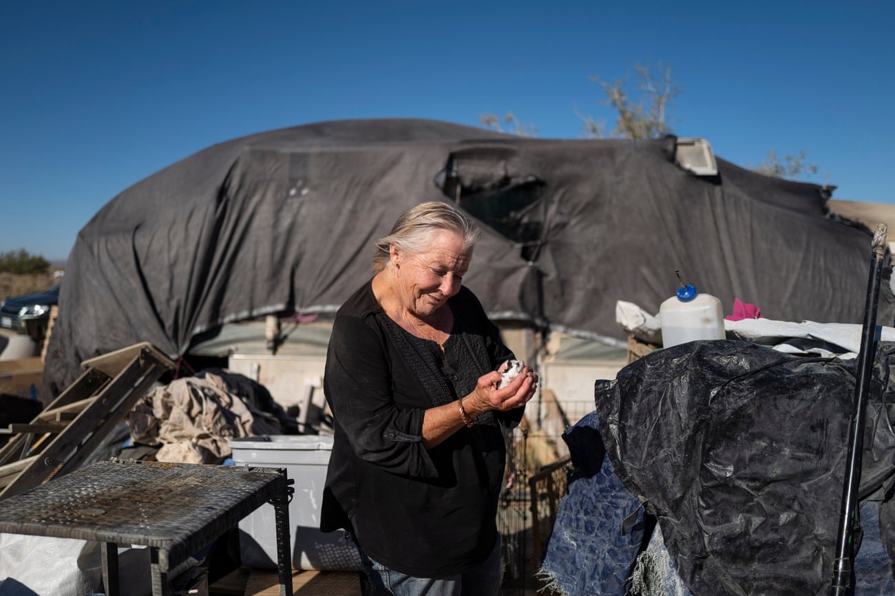 A woman holds her guinea pig in front of a makeshift shelter in the desert