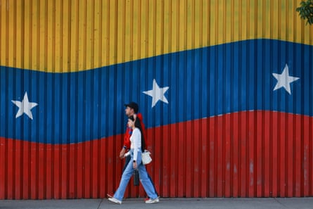 Un hombre y una mujer caminan frente a una pared pintada con los colores de la bandera nacional venezolana.