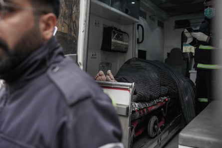The bare feet of a person protrude from beneath a blanket as they lay in the back of an ambulance