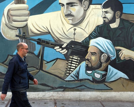 An Iranian man walks past a wall painting of Iranian soldiers in Tehran.