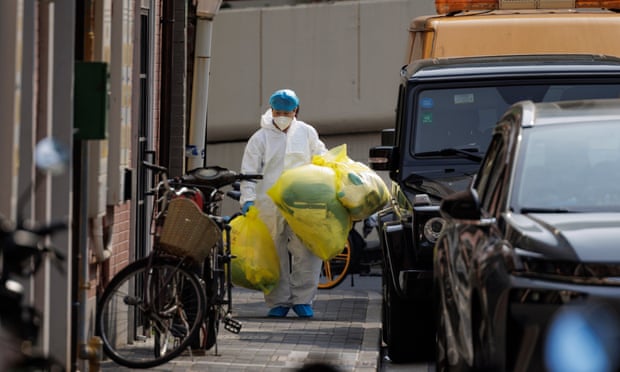 covid health worker walks in front of houses in china carrying waste bags