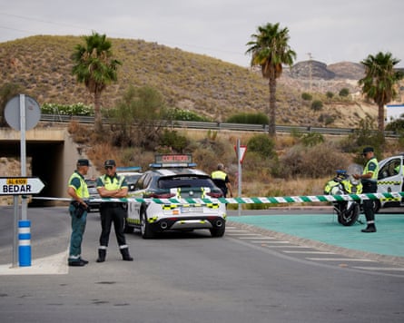 Police standing beside their cars behind cordon tape at a road junction in the hills of Alméria