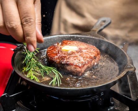 A person cooking a tenderloin steak in a pan with butter and herbs.