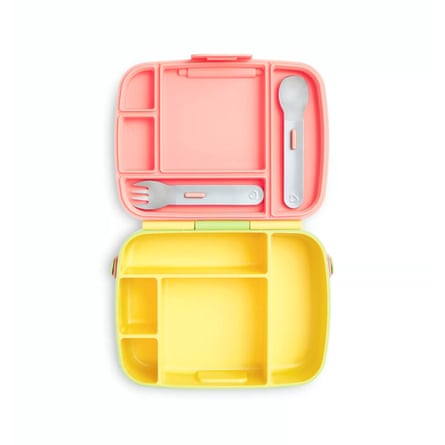 An open Munchkin Kids’ Bento Box Lunch Box with a yellow bottom and a pink top. In the lid there is a ford and knife clipped into place.