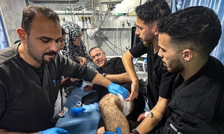 Hussam Abu Safiya is on a hospital bed. He appears to be wincing in pain as five colleagues treat his wounds. He has a bandage wrapped around his thigh