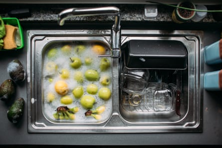 A sink of green apples, lemons and bananas being soaked in a bubbly, soapy-looking solution.
