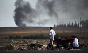 Men stand next to red motorbike watching smoke in the distance