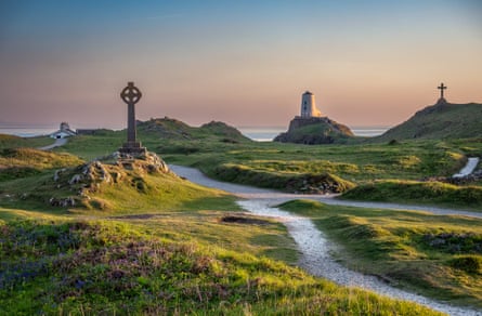 A Celtic cross stands in the left mid-ground, with a lighthouse and a second cross in the distance as dusk sets in