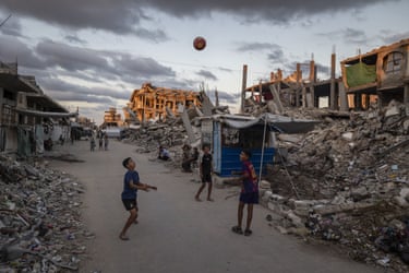 Children play football in a refugee camp amid the ruins