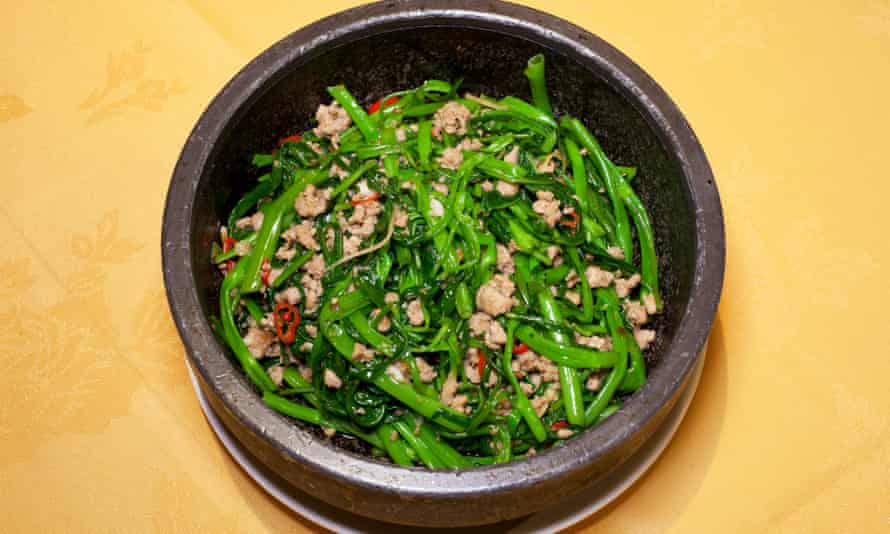 A thick round pot with morning glory, speckled with pieces of pork and chilli