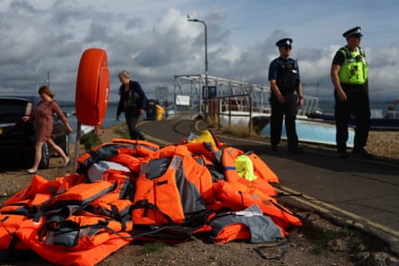 A pile of orange lifejackets by the road at Eastney Ferry Landing. Two police officers stand by.