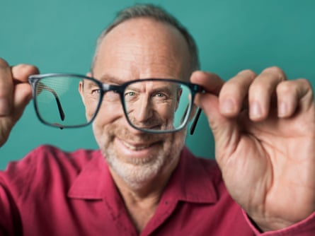 Portrait of Jimmy Wales holding his glasses away from his face so you can see him in focus through the glass