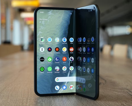 A Google Pixel 11 Pro Fold stands open in a V-shape, showing app icons across its internal tablet screen.