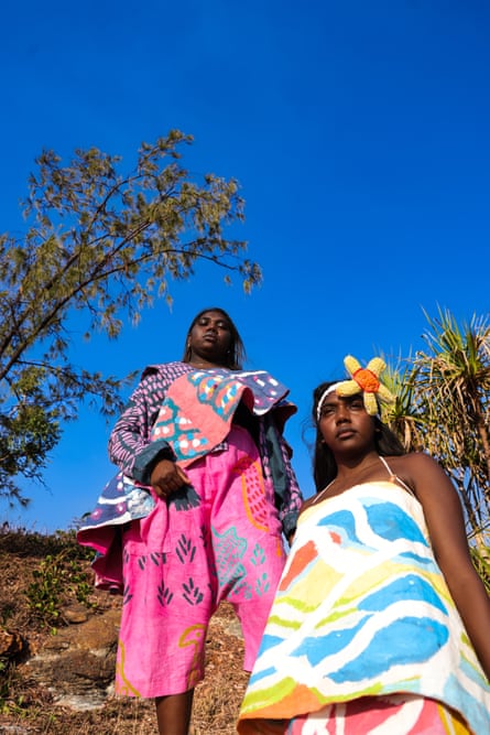 Women in brightly coloured outfits stand in the bush with a big blue sky in the background