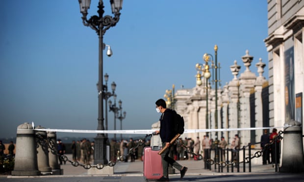 A man wearing protective mask pulls his suitcase in front of the Royal Palace in Madrid, Spain.