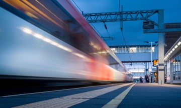 A LNER high speed train speeds through a railway station on the east coast main line, England, UK.