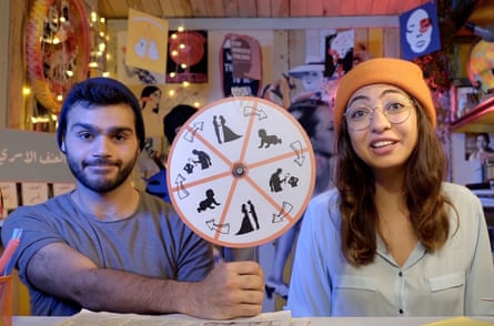 A man and a woman wearing beanie hats. The man is holding a wheel with images of a man and a woman; a baby; and a man with a child