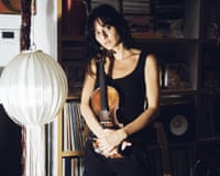 Singer Sofie Royer holds a violin, standing before a bookshelf and paper lantern lamp