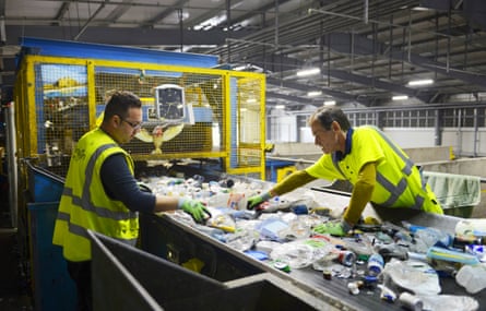 Two men in hi-vis sort a conveyor belt of rubbish including cans and plastic packaging.