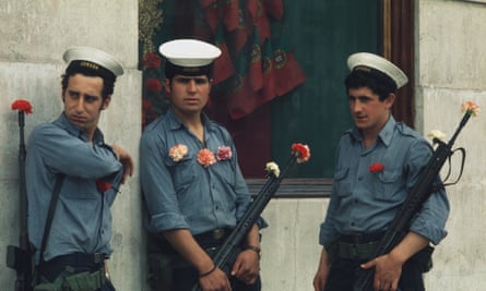 Portuguese soldiers with carnations on their uniforms and in their gun barrels lean on a building