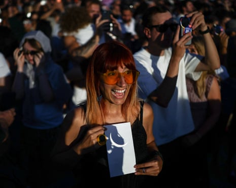 A woman holds a piece of paper showing the eclipse refracted from binoculars on Primrose Hill in London.