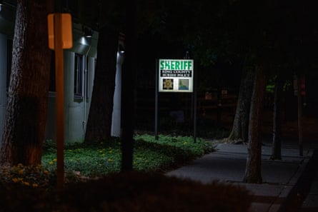 A sign that says, “Sheriff, King County, Burien Police,” is lit up at night outside a building. A few trees are near the sign.