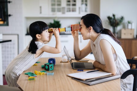 Young Asian mother working from home on laptop while little daughter playing with her on the desk.