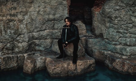 Jorge Rivera-Herrans sitting among rocks nestling a big sword.