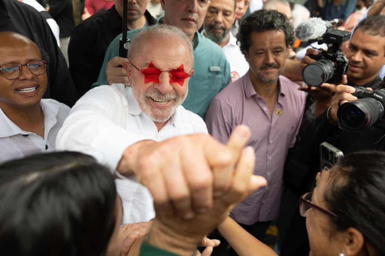 Man in red star-shaped sunglasses smiles while holding a supporter’s hand in crowd outside