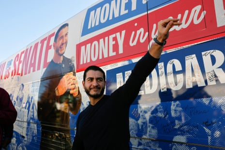 Man in black long-sleeve sweater waves in front of image of himself on side of bus.