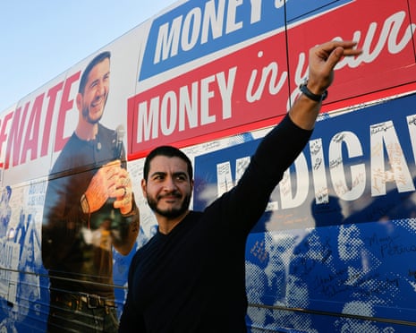 Man in black long-sleeve sweater waves in front of image of himself on side of bus.