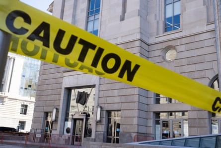 Barriers and warning tape surround a building whose sign has been covered with black plastic.