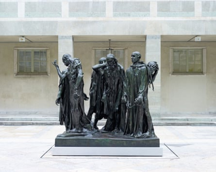 A large sculpture of multiple people set on a plinth standing in a courtyard