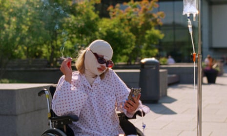 Kristine Kujath Thorp, in a wheelchair with bandaged face, checking her phone, in Sick of Myself.