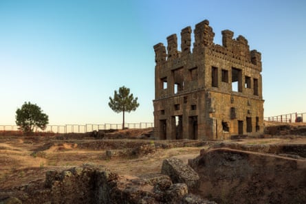 A tall, square, ruined building with two trees near it and a blue sky behind