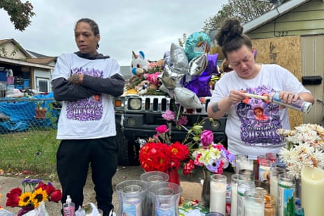 two people at memorial site with candles and flowers and matching T-shirts with child's photo