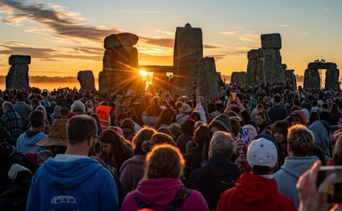 A large crowd of people watch as the sun rises between two of the monument's sarsen stones