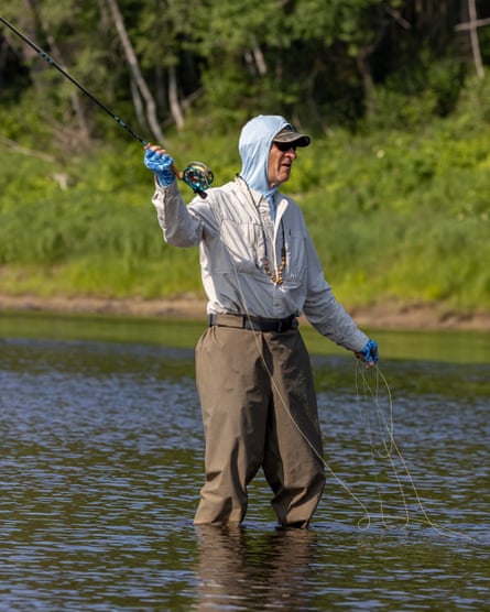 A man standing knee-deep in a river with a fishing rod in his hand