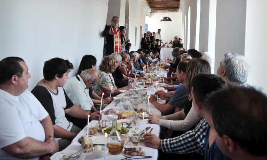 Un preot vorbește în timpul unei „cine de reconciliere” în Ktikados pe Tinos.  Sătenii, vizitatorii și turiștii sunt bineveniți să participe.