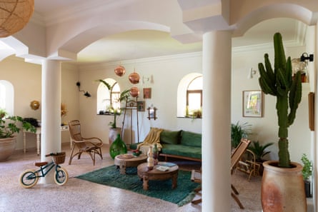 A living area, with arched windows to let in light, and internal arches and columns, a lounge and chairs, a child’s bike and an indoor cactus