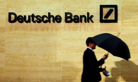 A man with an umbrella walks past Deutsche Bank offices in London